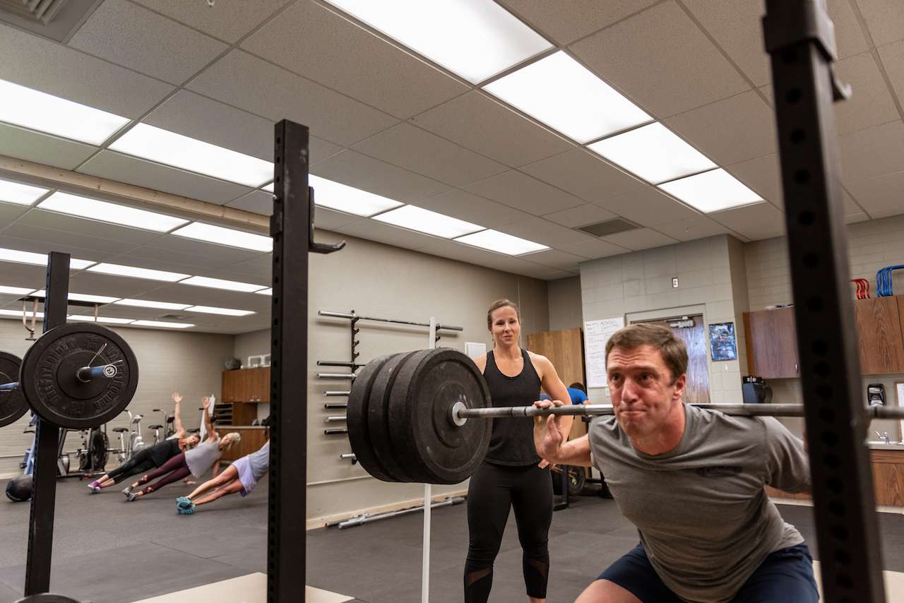 man doing squats with a barbell in front of a trainer