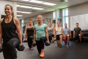 people in a group weight training class doing weighted lunges