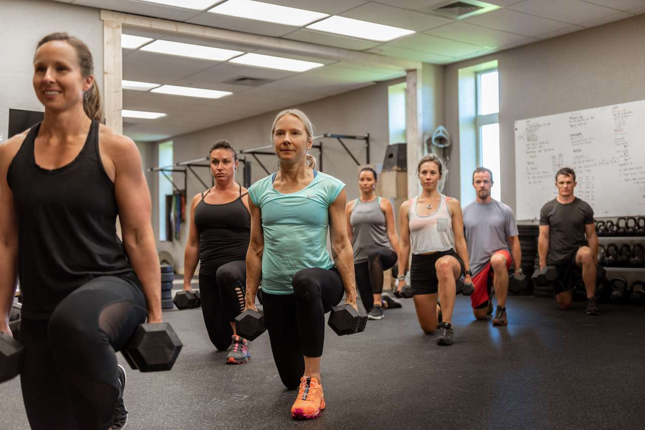 people in a group weight training class doing weighted lunges
